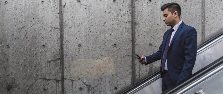 Ein Businessmann der auf einer Rolltreppe steht und währenddessen auf sein Handy starrt